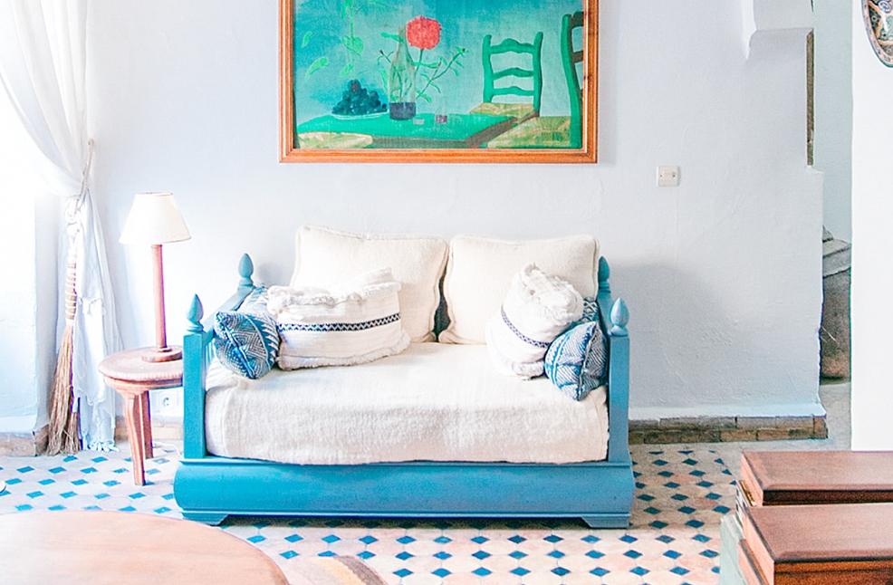 A blue sofa against a wall with a painting of a rose. The floor has a blue diamond pattern.