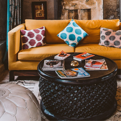 An orange couch with three cushions on top, and a coffee table in front of it with a few magazines on top of it.