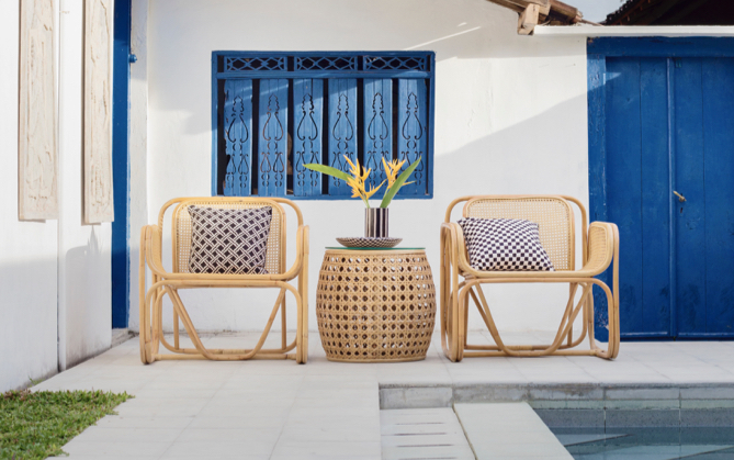 Two chairs near a pool separated by a wicker table that has flowers and a plate on it.